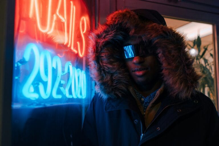 Man wearing. futuristic outfit, posing next to a neon sign.