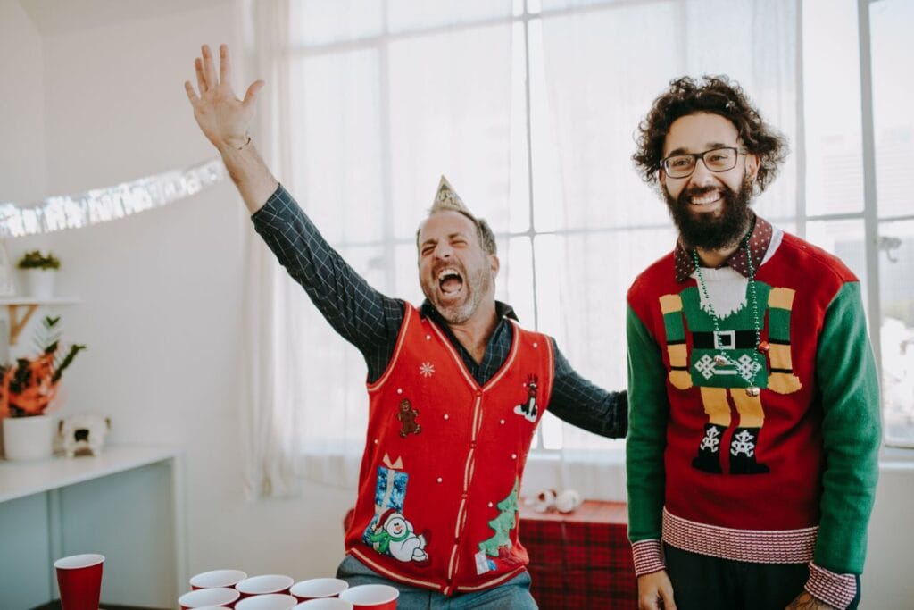 Two men in novelty jumpers celebrating at an ugly Christmas sweater party.
